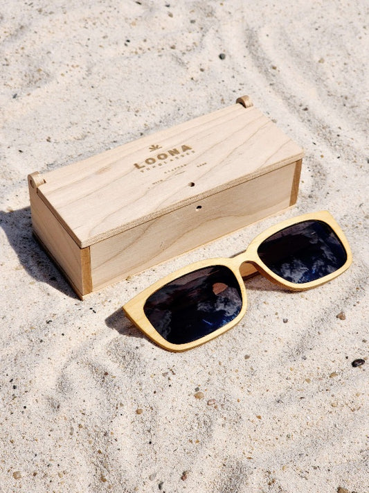 Maple wooden sunglasses with black polarized lenses and a box on sandy beach.