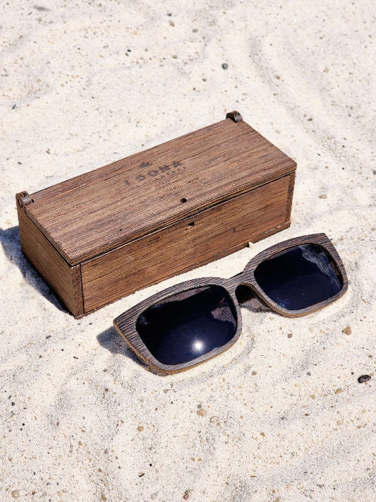 Wenge wooden sunglasses with black polarized lenses and a box on sandy beach.