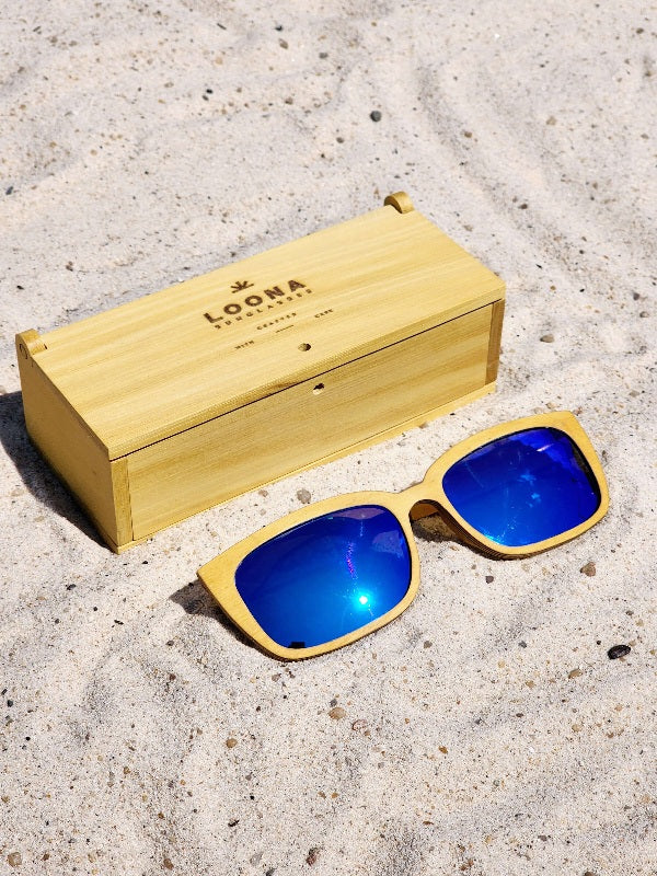 Yellowheart wooden sunglasses with blue polarized lenses and a box on sandy beach.
