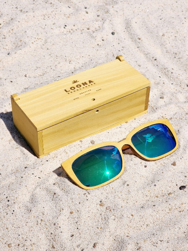 Yellowheart wooden sunglasses with green polarized lenses and a box on sandy beach.