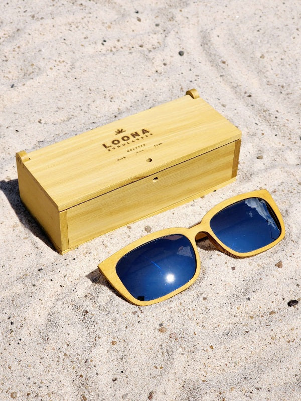 Yellowheart wooden sunglasses with silver polarized lenses and a box on sandy beach.