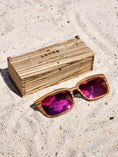Load image into Gallery viewer, Zebrawood wooden sunglasses with red polarized lenses and a box on sandy beach.
